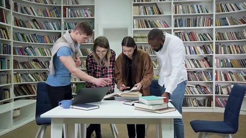 Vier zufriedene attraktive gemischtrassige Studenten stehen neben dem Bibliothekstisch und lesen ein Buch