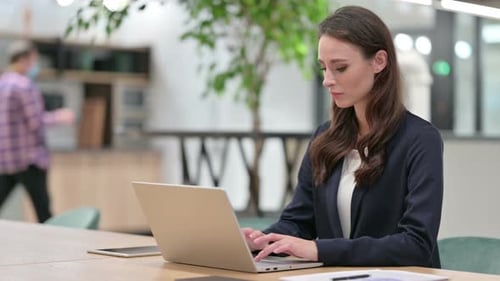 Young Woman Types on Laptop, Coughs in Office