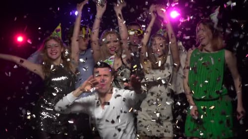 Companhia de amigos dançando sob confetes brilhantes. Câmera lenta