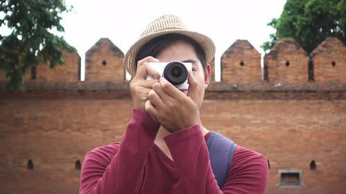 Smiling Man Taking Photos in Front of Brick Wall