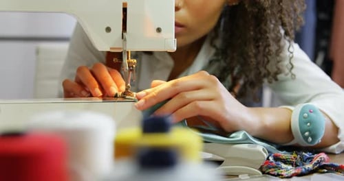 Front view of African American female fashion designer working with sewing machine in workshop 4k