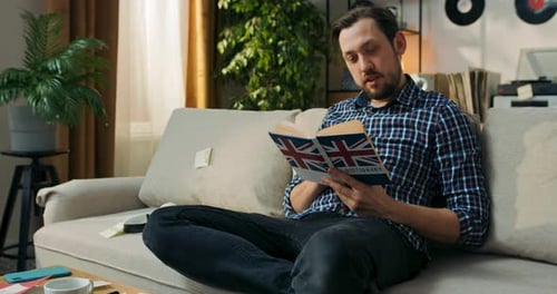 Man Sitting on Couch Reading English Dictionary