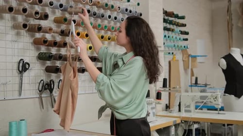 Concentrated femail tailor picking up threads under fabric color at workshop