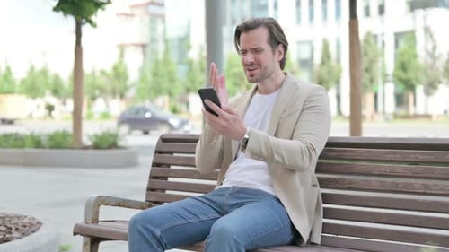 Man Reacting Negatively to Smartphone on City Bench