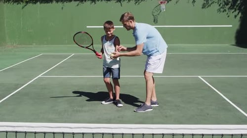 Caucasian father teaching his son to play tennis at tennis court on a bright sunny day