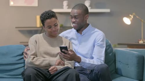 Smiling Couple Looking at Mobile Phone at Home