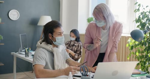 Colleagues Man and Woman Talking Looking at Laptop Screen Wearing Masks in Office
