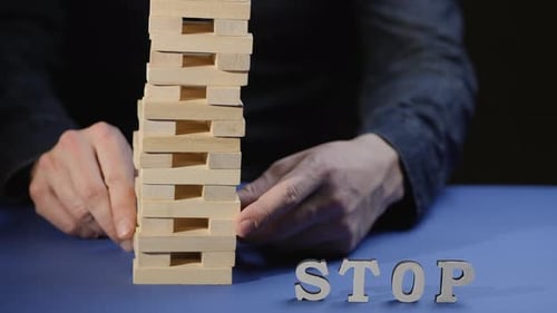 Une main masculine sort un bloc de bois et la tour s'effondre