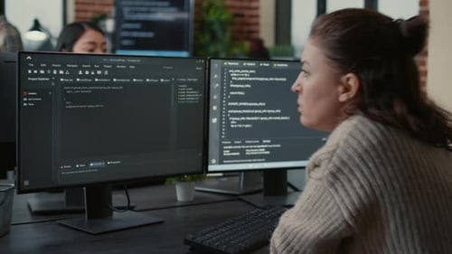 Focused Software Developer Writing Code Looking at Multiple Computer Screens