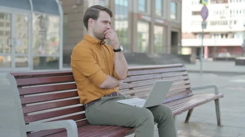 Thinking Young Man Using Laptop while Sitting Outdoor on Bench