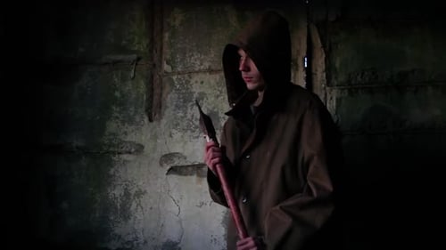 Silhouette of Man in Dark Cloak Walking Through Abandoned Building with an Ax