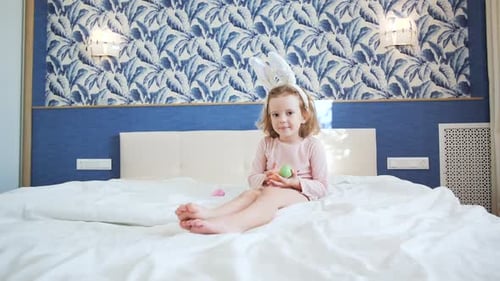 Ein süßes kleines Mädchen sitzt mit nach vorne gestreckten Beinen auf dem Kingsize-Bett
