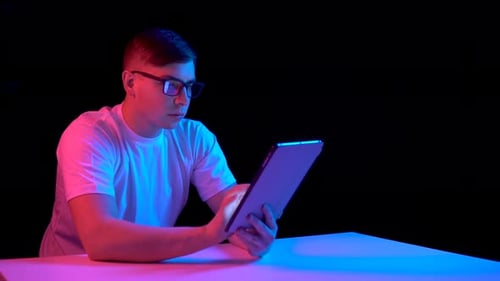 Hombre joven con una tableta. Un hombre usa una tableta. Una luz azul y roja cae sobre un hombre sobre un negro