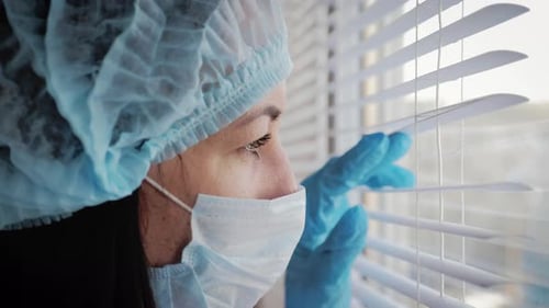 Concerned Woman in Medical Gear Looking Out Window