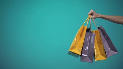 Hand Holding Shopping Bags Against Solid Background