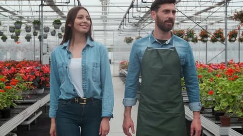 Smiling Gardeners Walking Through Flower-Filled Greenhouse
