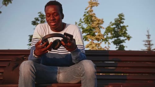 Ein junger schwarzer Student in stylischer Kleidung sitzt und spricht auf einem Smartphone in der Stadt
