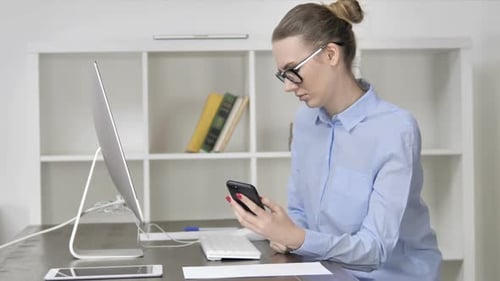 Young Casual Girl Using Smartphone While Working on Computer