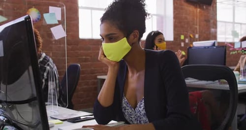 Woman Works on Computer in Busy Office Wearing Mask