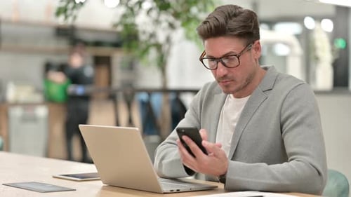 Adult Man Using Cellphone and Laptop in Office