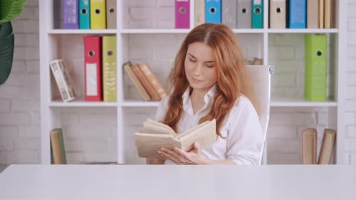 Woman Reading Book at Desk in Bright Office