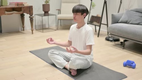 Young Adult Meditating on Yoga Mat at Home