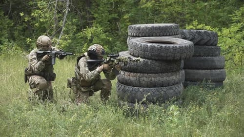 Soldiers Crouching Behind Tires Aiming Rifles in Field