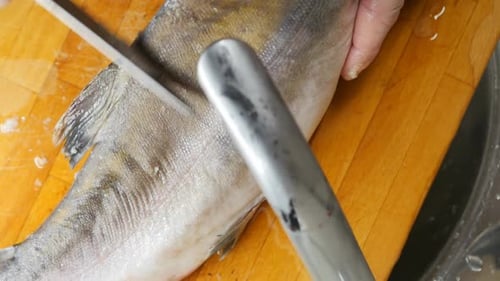 le chef épluche les écailles du poisson sur la planche dans l'évier avec un couteau