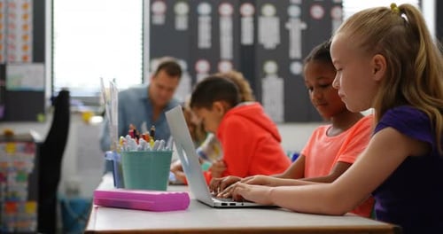 Vue latérale d'écolières métisses étudiant sur un ordinateur portable dans la salle de classe 4k