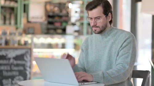Man Typing on Laptop Massaging Neck Indoors