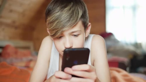 Teenage Boy Using Smartphone Lying in Bed