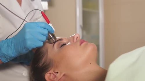 Kosmetikerin bereitet das Gesicht einer Frau auf eine Mesotherapie-Behandlung ohne Injektion vor