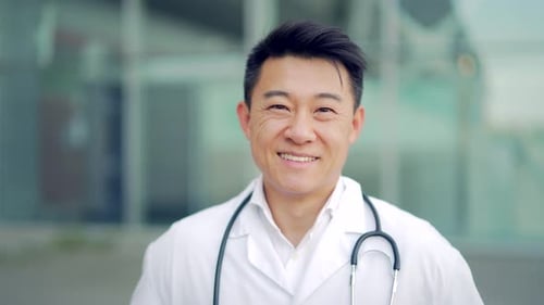 Close up portrait of Asian doctor looking at camera with arms crossed on background