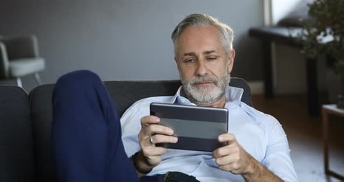 Mature Man Relaxing on Couch with Tablet