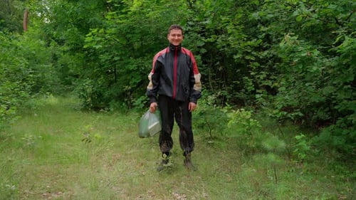 Hombre recoge basura en el bosque en un paquete, mirando a la cámara sonriendo
