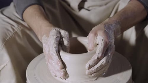Les mains masculines du potier façonnent et sculptent le pot en argile blanche tendre qui tourne sur un volant de potier dans un