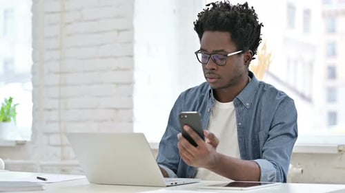 Young Adult Using Phone and Laptop at Desk
