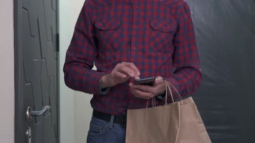 El servicio de mensajería se para en la puerta del apartamento del cliente con la comida y llama al cliente.