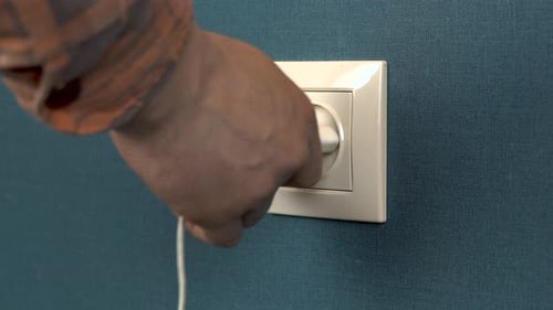 A Man Plugs a Phone Charger Into a Wall Outlet. Rosette in the Wall with Dark Blue Wallpaper