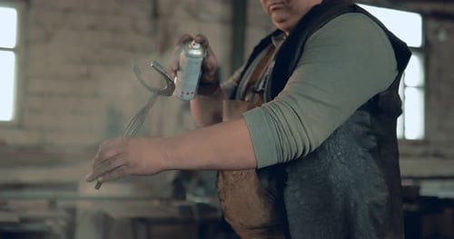 Man Spraying Metal Clamps with Lubricant in Workspace