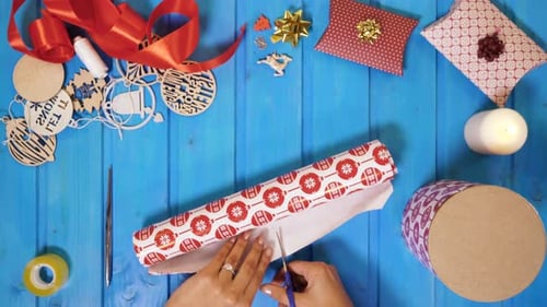 Hands Wrapping Christmas Gifts With Scissors on Blue