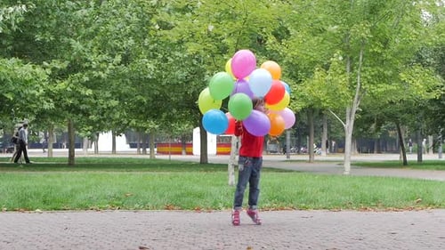 Little Girl Jumps with Colorful Balloons in Park