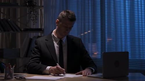 Man in Suit Writes at Desk at Night