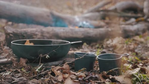 Cooking on a Campfire on a Hike. A Girl Prepares Eggs with Tomatoes and Bacon in a Pan on a Campfire