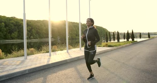Woman Jogging on Path near Lake at Sunrise
