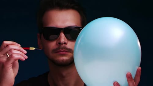 Man with Sunglasses Pops Balloon with Dart