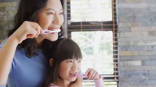 Woman and Girl Brush Teeth in Bathroom