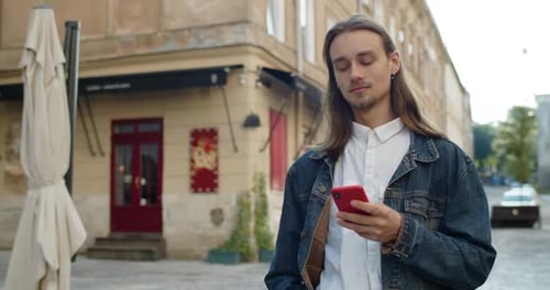 Long Haired Man Using Smartphone on City Street