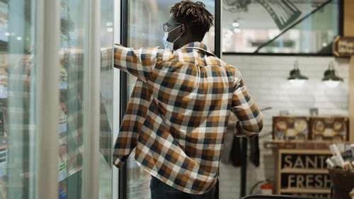 African American Shopper Selects Food in the Fridge of a Grocery Store