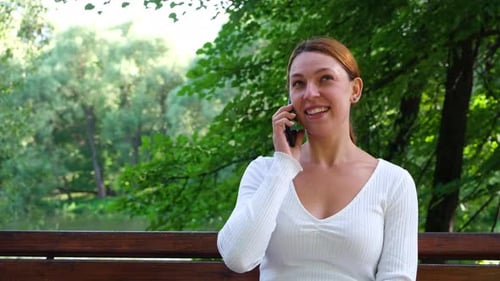 Pretty Woman Talking on Mobile Phone on the Background of the Park.